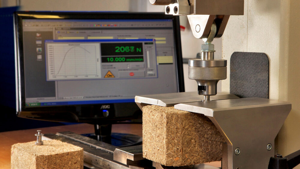 A composite block under load in the Eirebloc laboratory test rig, with the reading shown on screen.