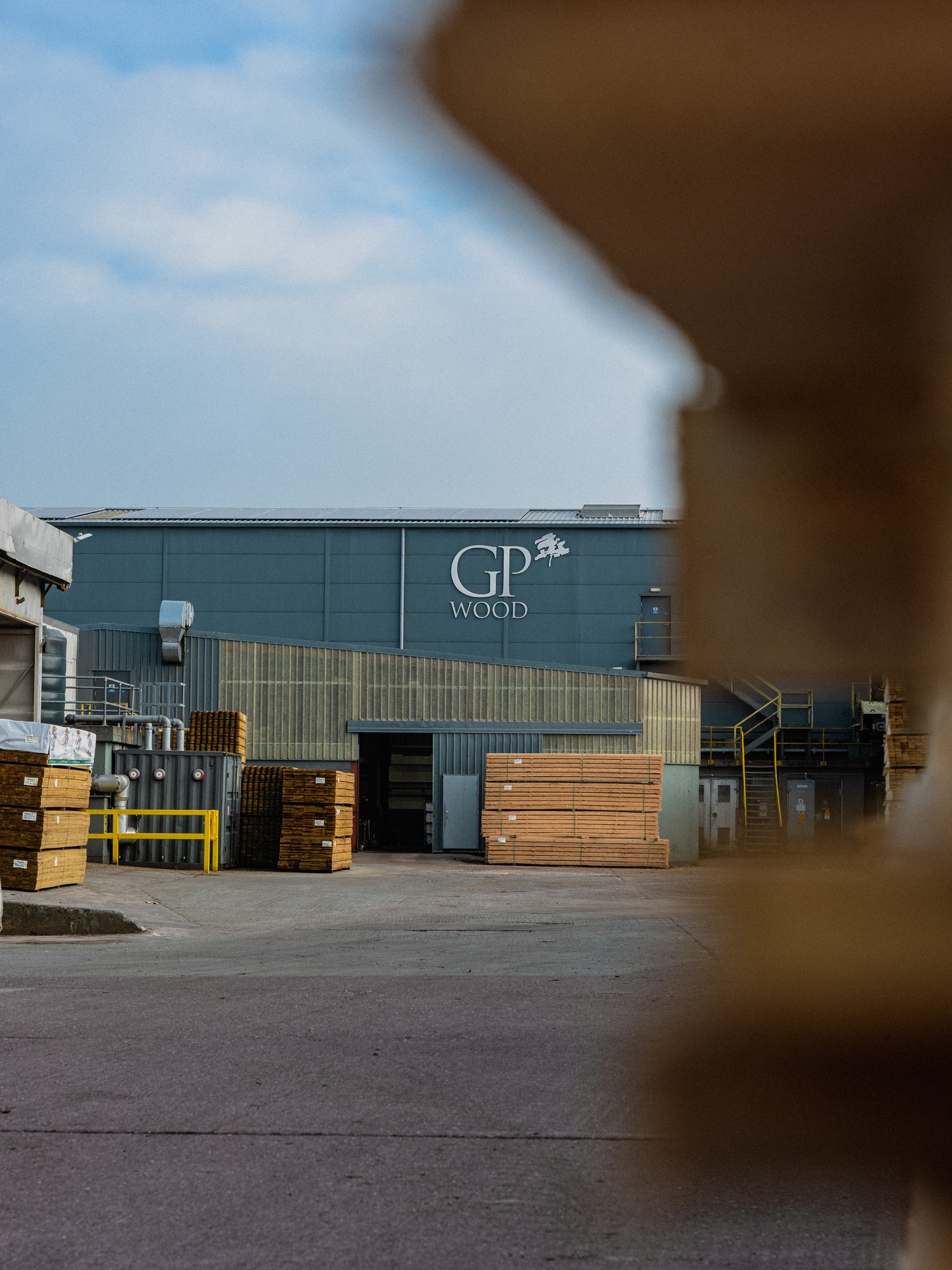 The GP Wood sawmill building with packs of sawn timber stacked in the yard, seen past a timber pack in the foreground.