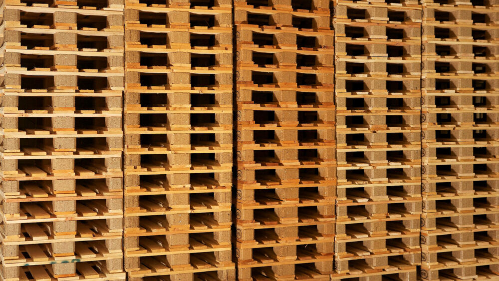 Tall stacks of new wooden pallets built with composite blocks, seen from the side.